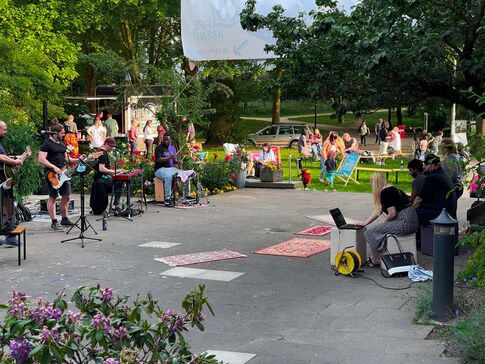 Menschen sitzen und stehen im sommerlichen Park, es spielt eine Band.