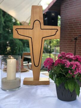 Ein Holzkreuz, eine Kerze und ein Blumentopf auf einem Altar im Freien.