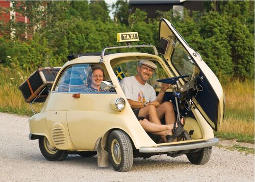 Ein Paar in einer cremefarbenen Isetta mit Taxi-Schild auf dem Dach.