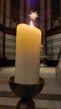 Eine brennende Kerze in einer Kirche, im Hintergrund ein leuchtender Herrenhuter Stern.