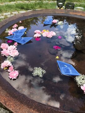 Schwimmende Blüten und Kerzen in Bootform auf einer Wasserschale.
