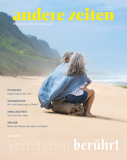 Der Titel des Magazins zum Kirchenjahr zeigt zwei Menschen auf einem Baumstumpf am Strand, gemeinsam in ein Handtuch eingehüllt