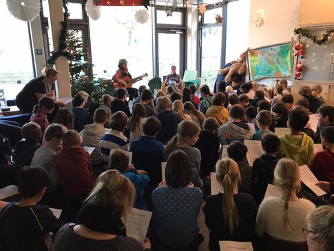 Kinder von hinten, im Hintergrund spielt eine Frau Gitarre