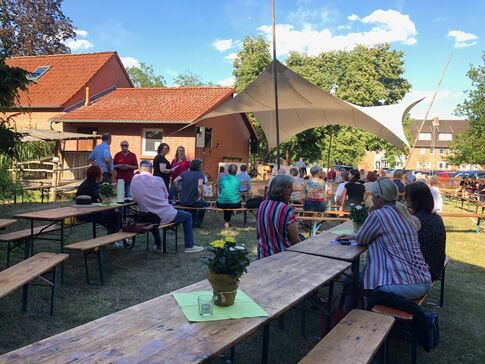 Menschen an Biertischen vor einer Bühne in einem Garten.