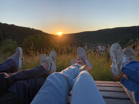 Vier Paar Füße auf einer Bank vor dem Sonnenuntergang in der Eifel.