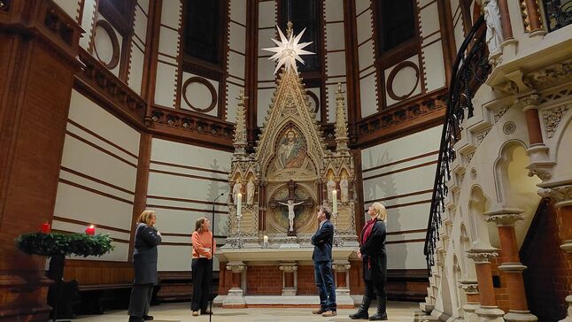Vier Menschen im Altarraum einer Kirche, über ihnen ein leuchtender Herrenhuter Stern.