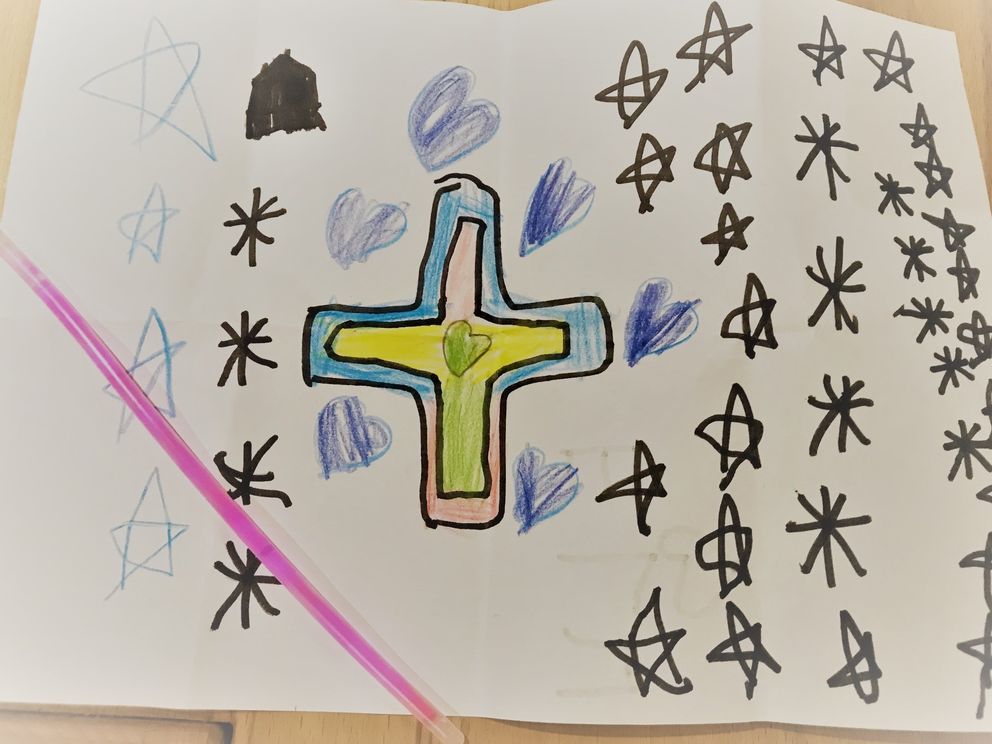 Ein Kreuz mit Herzen und Sternen darum herum, auf dem Bild liegt ein pinker Leuchtstab.