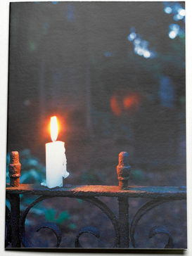 Eine brennende Kerze auf einem Zaun in der Dunkelheit
