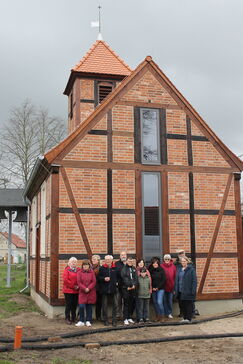 Eine Gruppe von Menschen steht vor einer Fachwerkkapelle.