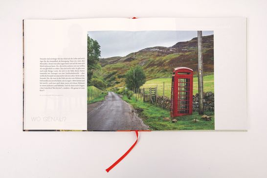 Eine Doppelseite aus dem Buch, links Text, rechts eine rote Telefonzelle auf dem Land in Großbritannien