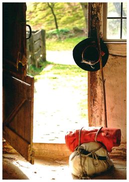 Ein Wanderbündel und ein Stock sowie ein Wanderhut neben der Haustür einer Hütte