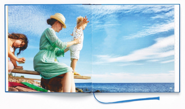 Die Doppelseite zeigt eine Frau mit zwei Kindern am Meer. Das jüngere Kind steht auf einer Holzplanke über dem Wasser und streckt die Arme aus. Die Frau hält es fest.