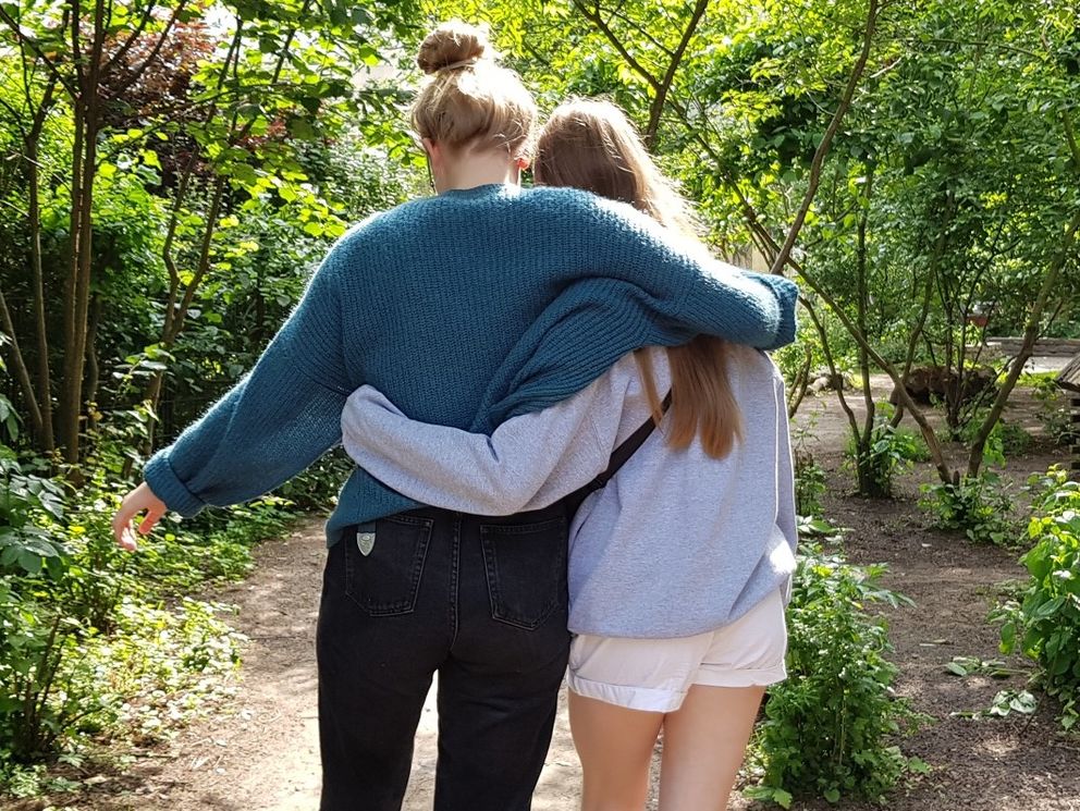 Zwei junge Mädchen gehen Arm in Arm durch einen Park.