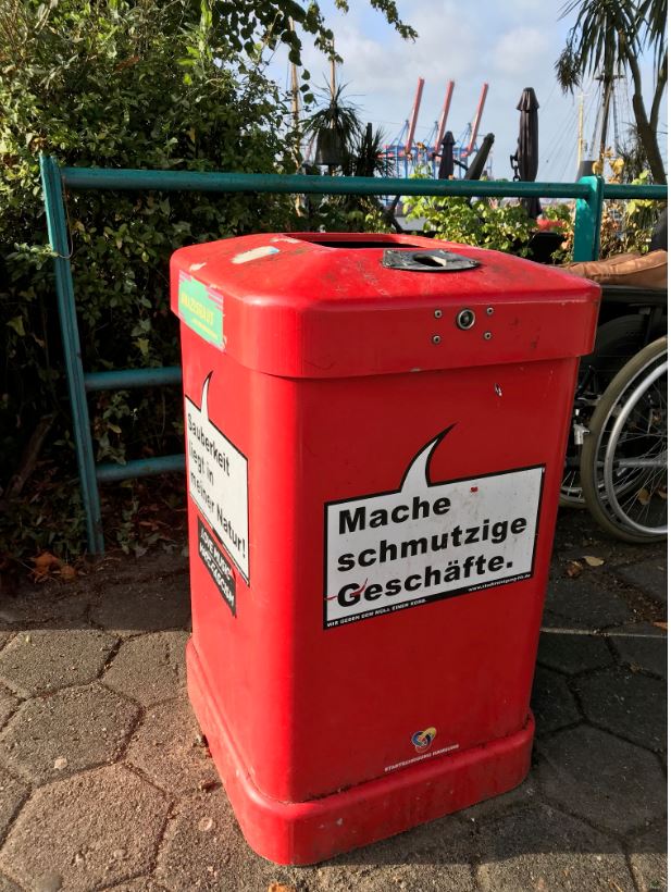 roter Mülleimer mit der Aufschrift "Bin für jeden Dreck zu haben", im Hintergrund Hafenkräne